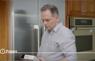 MAN EXAMINES AUTOMATED MINI-DOSER BOX WHILE STANDING IN FRONT OF FRIDGE MAN EXAMINES AUTOMATED MINI-DOSER BOX WHILE STANDING IN FRONT OF FRIDGE