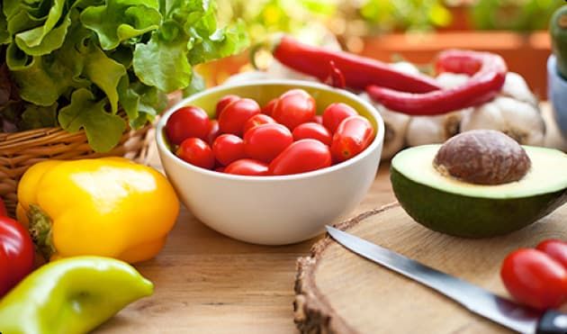 BOWL OF CHERRY TOMATOES, HALF AVOCADO, GARLIC, LETTUCE, PEPPERS ON A COUNTER